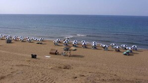 Une plage bordée de rangées de parasols et de chaises longues, une tour de surveillance des sauveteurs, et l’océan en arrière-plan.