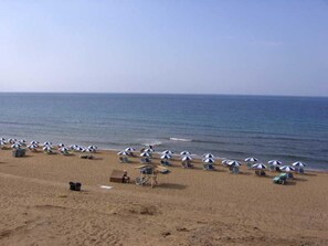 A beach with rows of umbrellas and beach chairs, a lifeguard tower, and the ocean in the background. - Blue Diamond Studios (Corfu)
