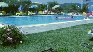 Une piscine entourée de verdure, avec des chaises longues et des parasols, sous un ciel dégagé.