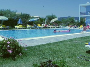 A swimming pool with lounge chairs and umbrellas, surrounded by greenery and a clear sky. - Blue Diamond Studios (Corfu)
