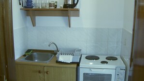 A compact kitchen with a sink, a stove, and a shelf above the sink holding a kettle and cups. - Blue Diamond Studios (Corfu)