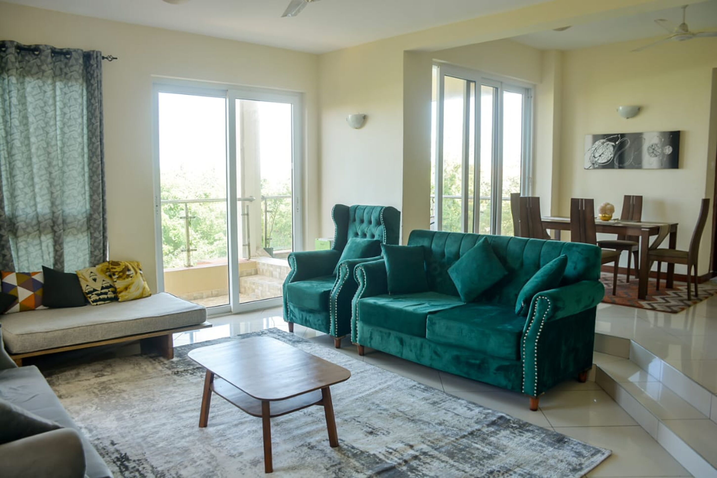 A living room with a sofa, a green velvet sofa, a wooden coffee table, and a dining area with a table and chairs.
