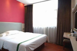 Une chambre d’hôtel avec un lit, un bureau et une fenêtre avec des rideaux.
