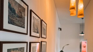 A hallway with framed pictures on the wall, a seating area with a table and chairs, and hanging pendant lights. - Charming condo at the heart of Batroun old souk (Batroun)