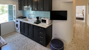 A modern kitchen with dark cabinets, a built-in microwave, and a washing machine. There are pendant lights and a large window. - Charming condo at the heart of Batroun old souk (Batroun)