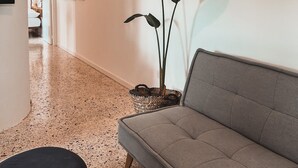 A modern living room with a grey sofa, a coffee table, and a potted plant. There is a TV mounted on the wall and a framed picture collection. The floor is speckled, and the room has a clean, minimalist design. - Charming condo at the heart of Batroun old souk (Batroun)