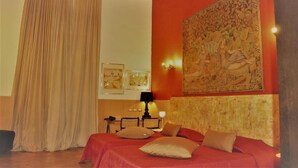 A hotel room with a bed, a desk, a lamp, and a large tapestry on the wall. - Costantinapoli 27 (Naples)