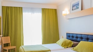 A hotel room with two beds, a chair, and a window with curtains. - Pontalaia Apartamentos Turisticos (Vila do Bispo)