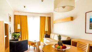 A modern living room with a round wooden table, a sofa, and a dining area. - Pontalaia Apartamentos Turisticos (Vila do Bispo)
