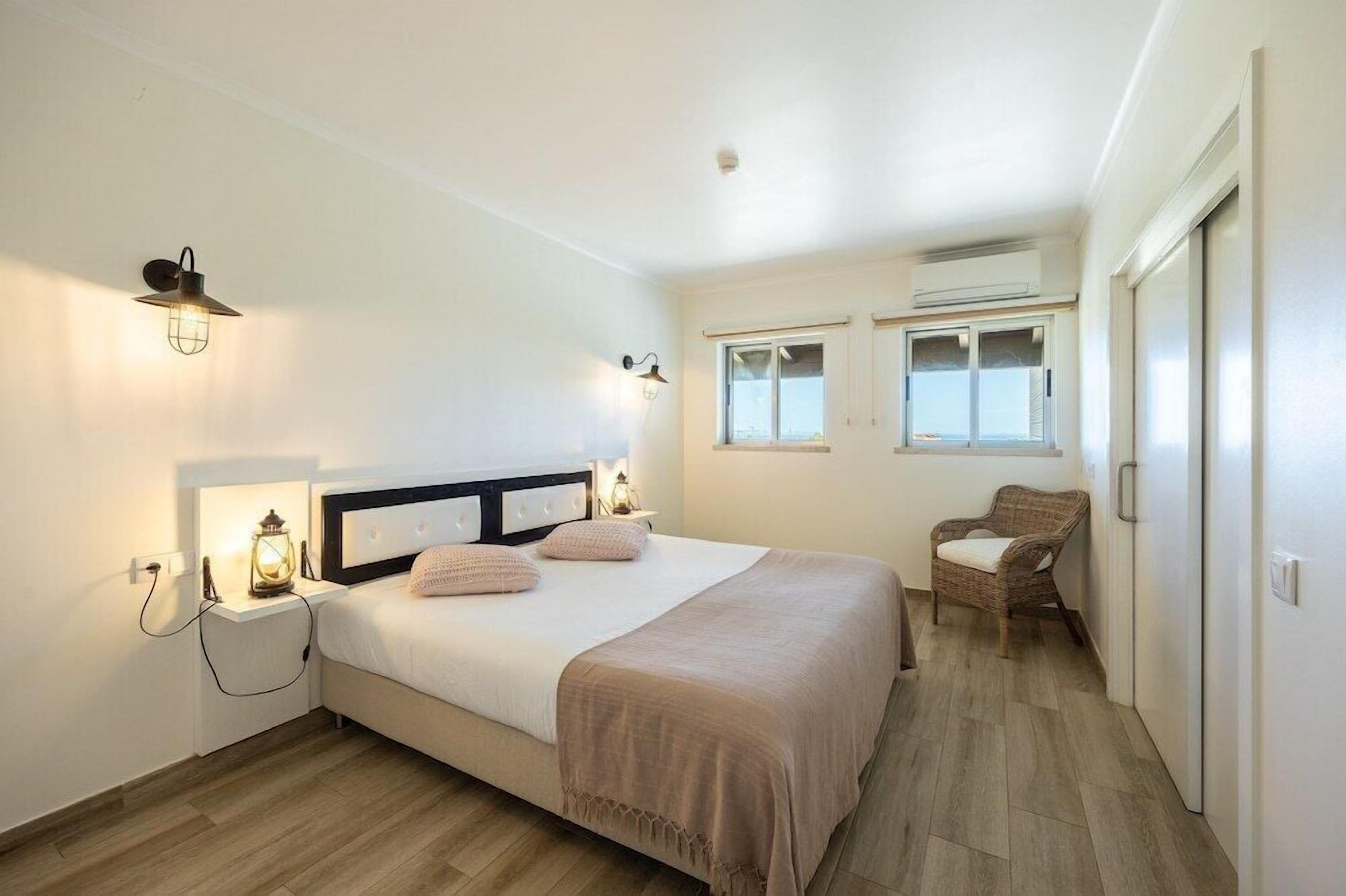 A bedroom with a bed, bedside lamps, a chair, and a window.