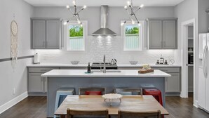 A modern kitchen with grey cabinets, a white island, and a dining area with wooden chairs.