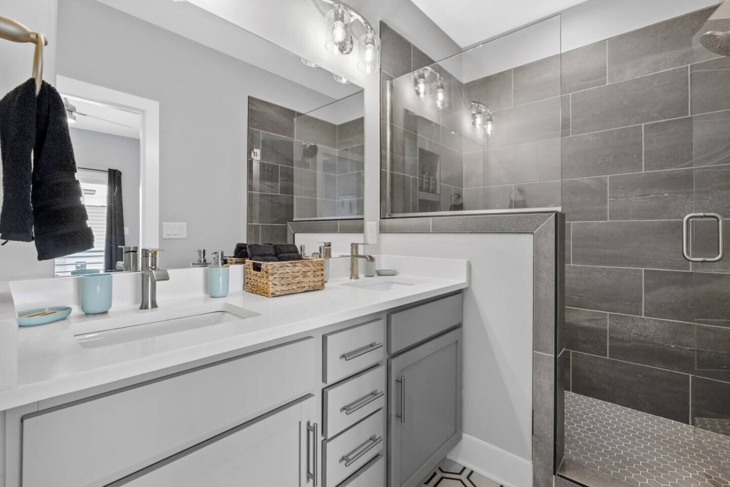 Een moderne badkamer met een wit wastafelmeubel, een douchecabine met glazen wanden en grijze betegelde wanden.
