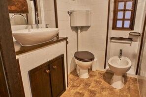 A bathroom with a large vessel sink, a toilet, and a bidet.