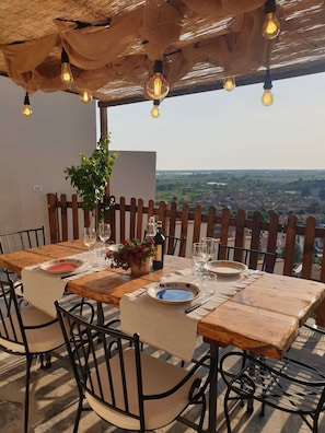 An outdoor dining area with a table set for two, surrounded by metal chairs, under a thatched roof with hanging light bulbs. - House Chez Paul (Massarosa)