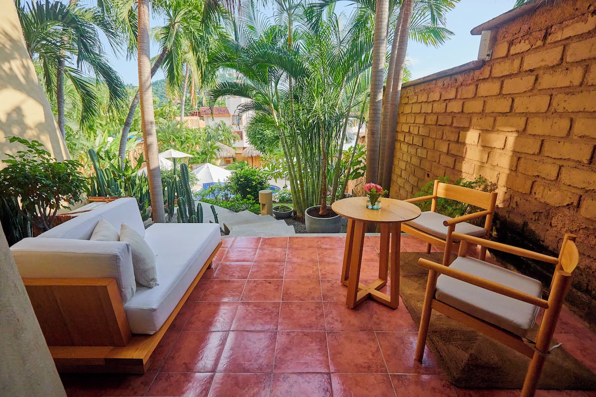 Un espace patio avec un canapé blanc, des chaises en bois, une petite table ronde et un mur en briques.