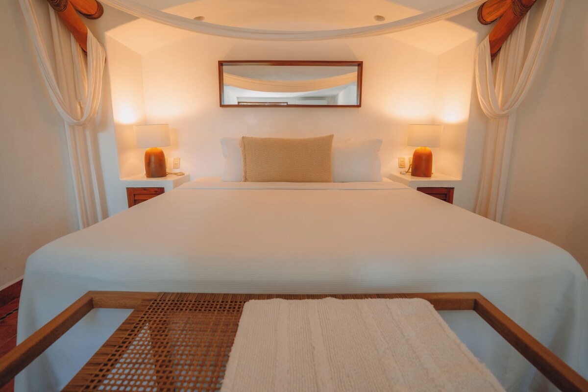 A bedroom with a large bed, two bedside lamps, a mirror, and a wooden headboard.