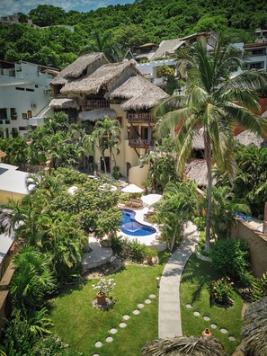 A resort with a swimming pool, thatched-roof buildings, and lush greenery. - La Villa Luz (Zihuatanejo)