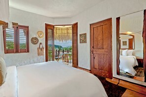 A bedroom with a large bed, wooden doors, and a view of the outdoors.