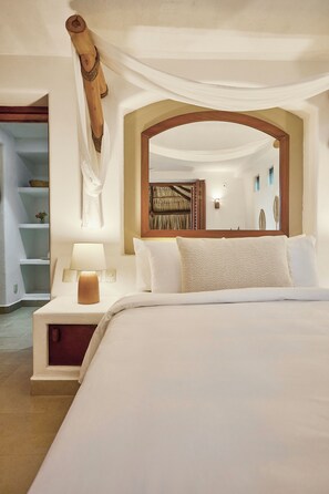 A neatly arranged bedroom with a large bed, a bedside table with a lamp, and a mirror above the bed.