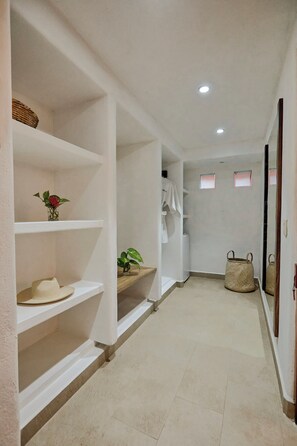A hallway with white walls, shelves with various items, a mirror, and a door. - La Villa Luz (Zihuatanejo)