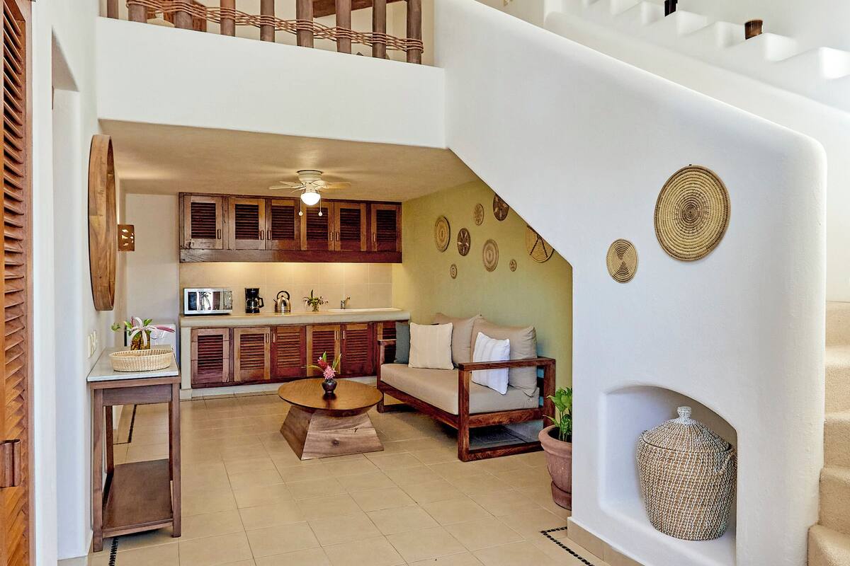 Un amplio salón con techo alto, una escalera, una cocina y una zona de estar.