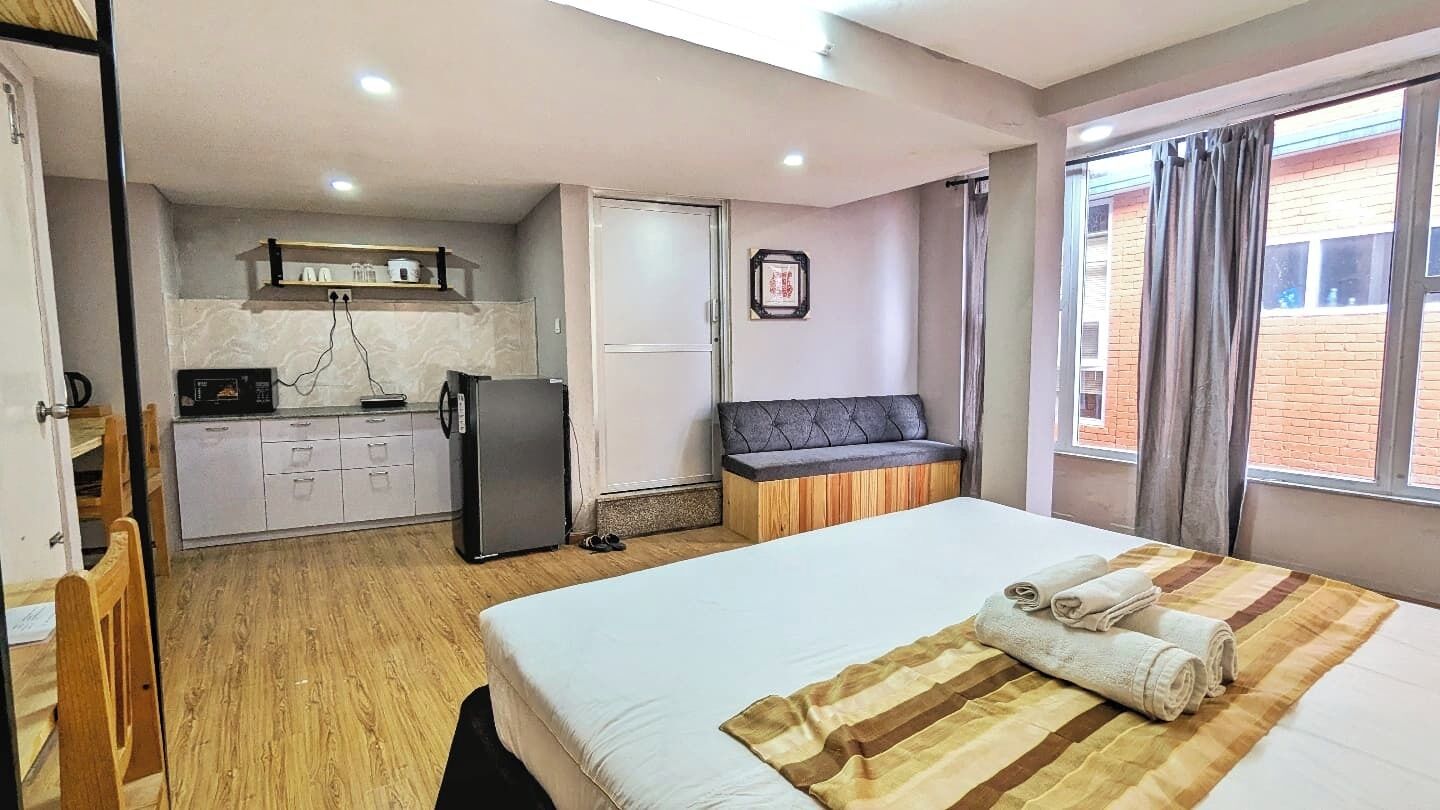 A hotel room with a bed, a small kitchenette, a sofa, and a window with curtains.