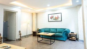 A modern living room with a teal sofa, a wooden coffee table, and a framed floral artwork on the wall. - Nyadha House (Lalitpur)