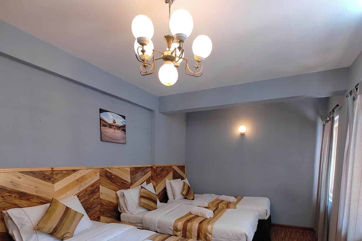 A hotel room with two beds, wooden headboard, a chandelier, a painting on the wall, and a window with curtains.