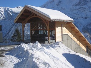 A wooden mountain lodge with a snow-covered roof, a staircase leading up, and a view of snow-capped mountains in the background. - Noemys pra Palier (Orcieres)