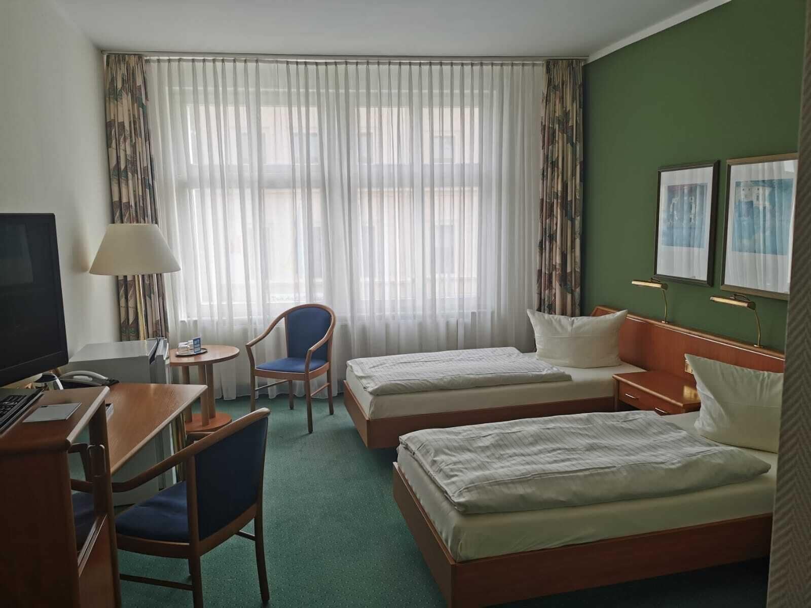 Habitación de hotel con dos camas, un escritorio con computadora, una silla y un televisor.