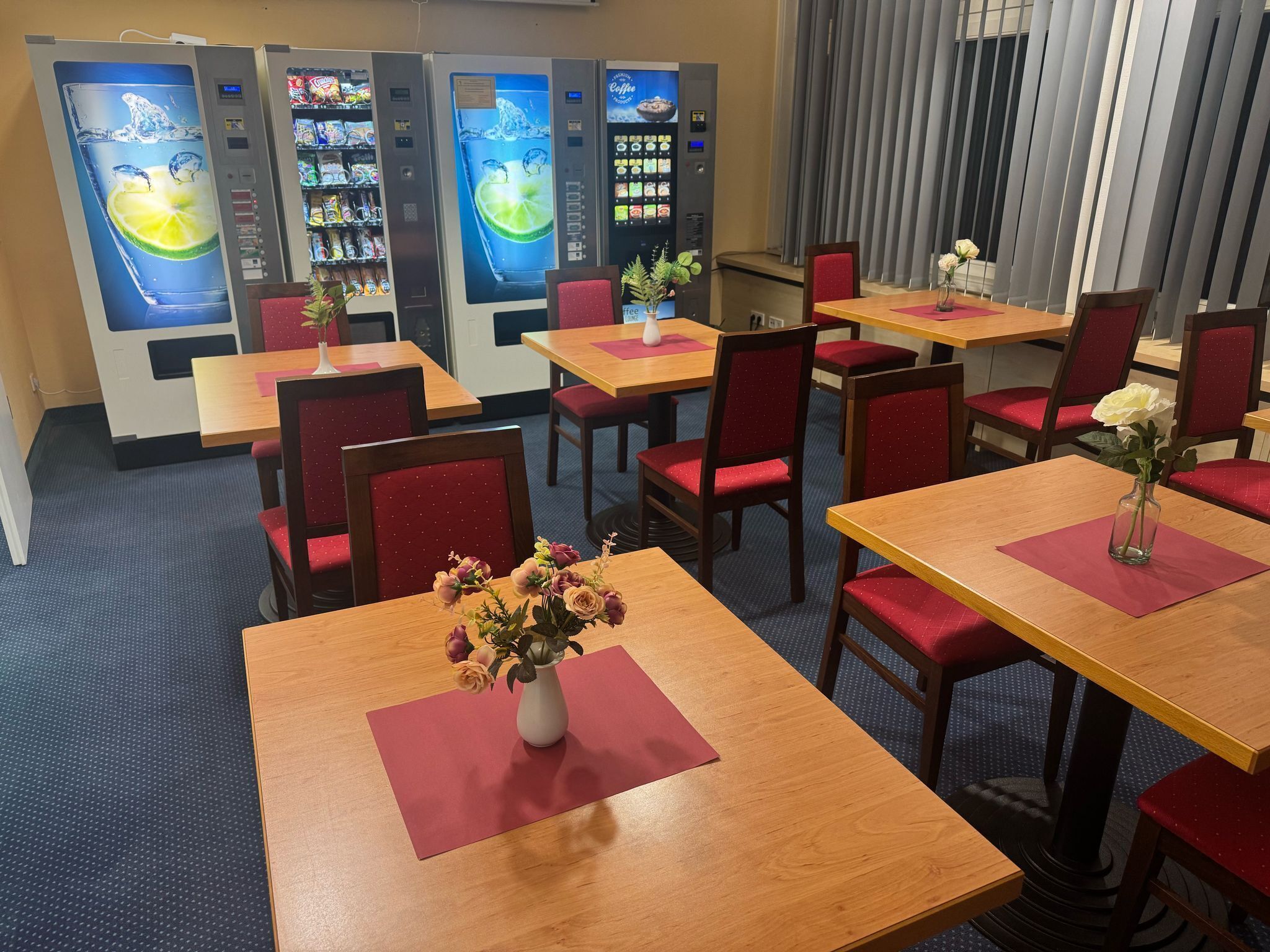A restaurant with multiple tables, red cushioned chairs, and vending machines in the background.