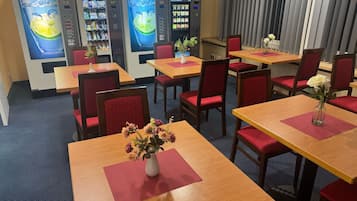 A restaurant with multiple tables, red cushioned chairs, and vending machines in the background.