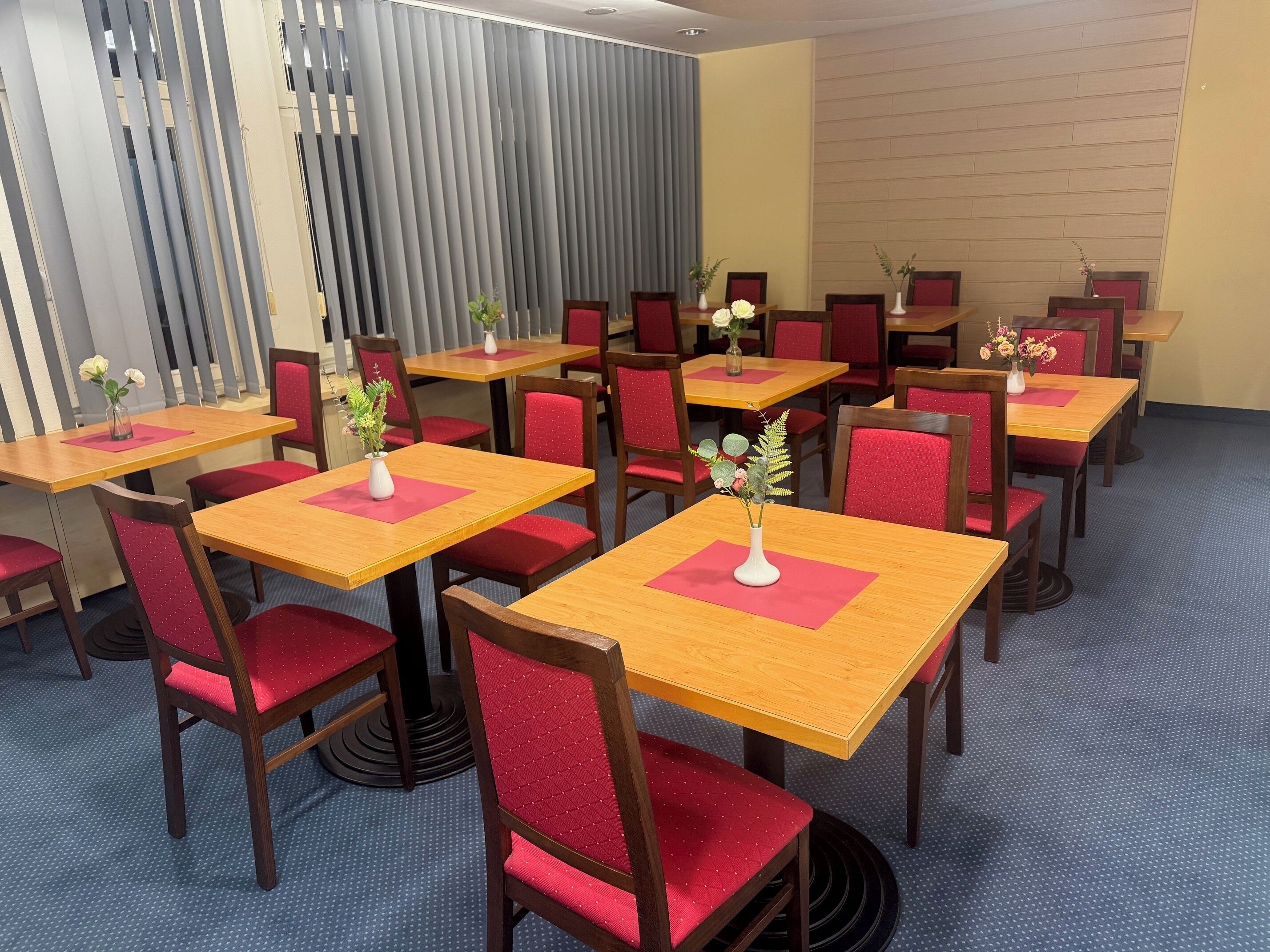 A hotel dining area with multiple tables and chairs, each with a vase of flowers.