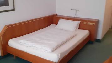 Una cama individual con cabecera y piecera de madera, ropa de cama blanca y una mesita de noche con una lámpara.
