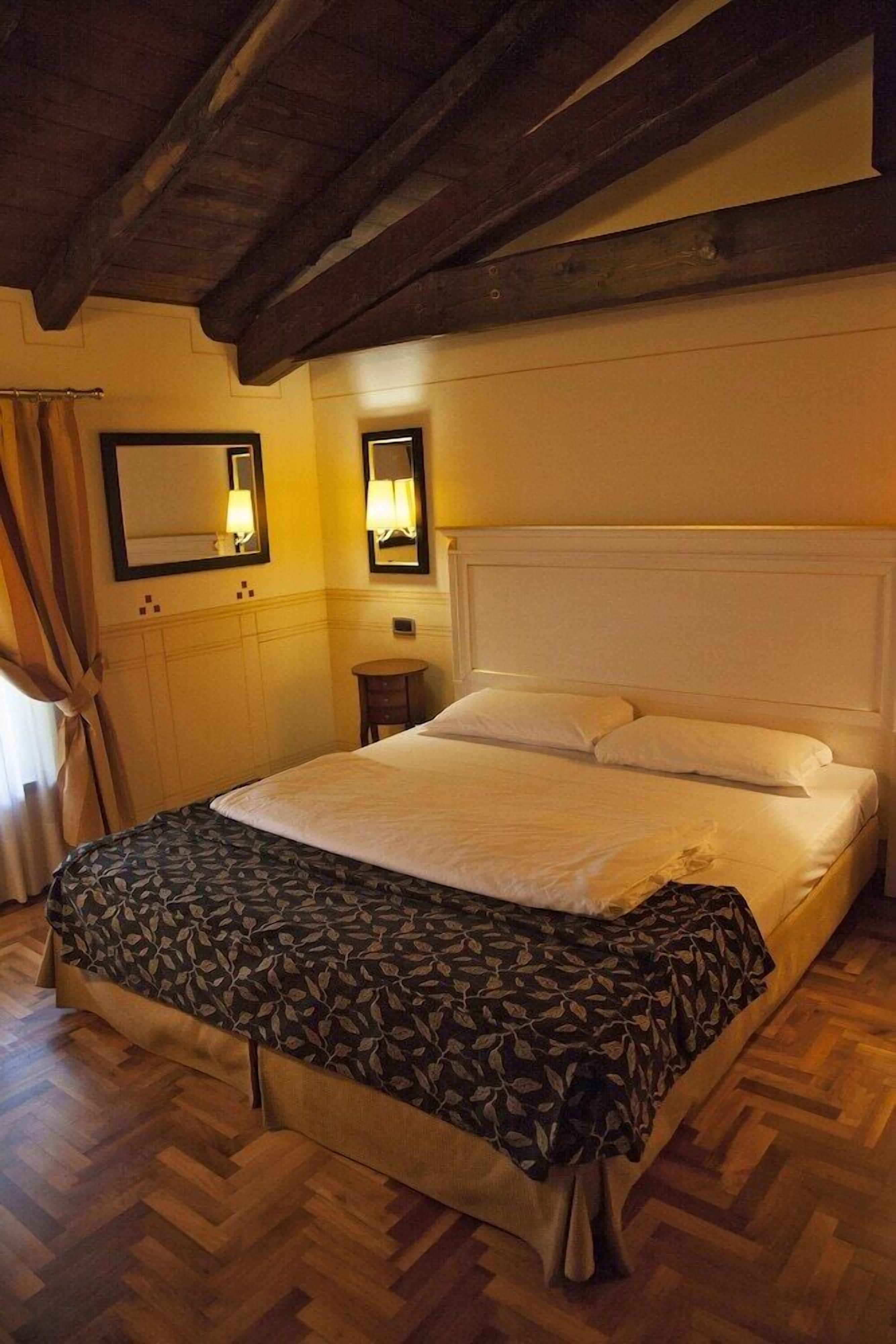 Ein Hotelzimmer mit einem großen Bett, Holzboden und einer hohen Decke mit freiliegenden Balken.