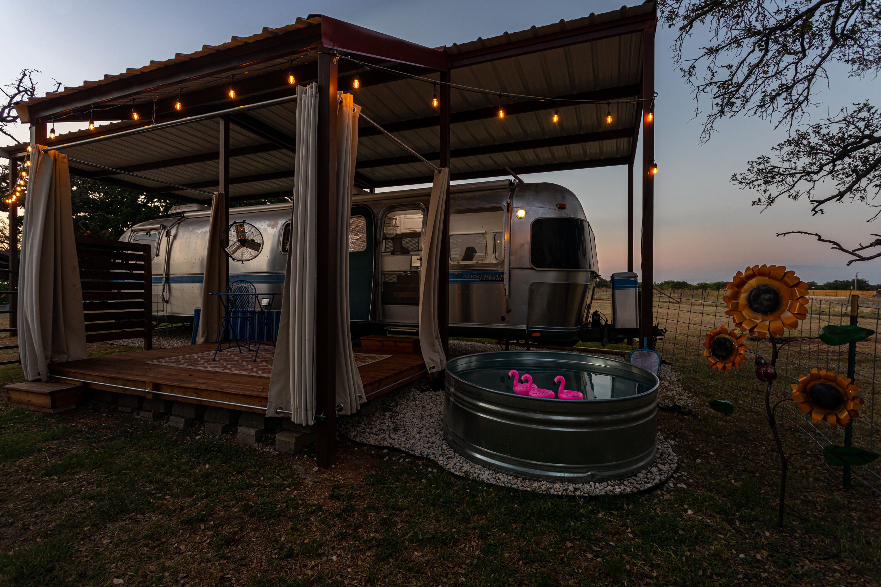 A covered outdoor area with a pool, a camper van, and a gazebo with string lights.