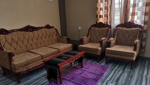 Un salon comprenant un ensemble de canapés, deux fauteuils, une table basse et un tapis violet.