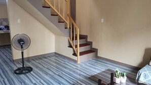 Une pièce dotée d’un sol en marbre, d’un escalier en bois, d’un ventilateur sur pied et d’un lit recouvert d’une couvre-lit à motifs.