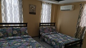 Une chambre avec deux lits, des rideaux à motifs, un appareil de climatisation et un élément décoratif mural.
