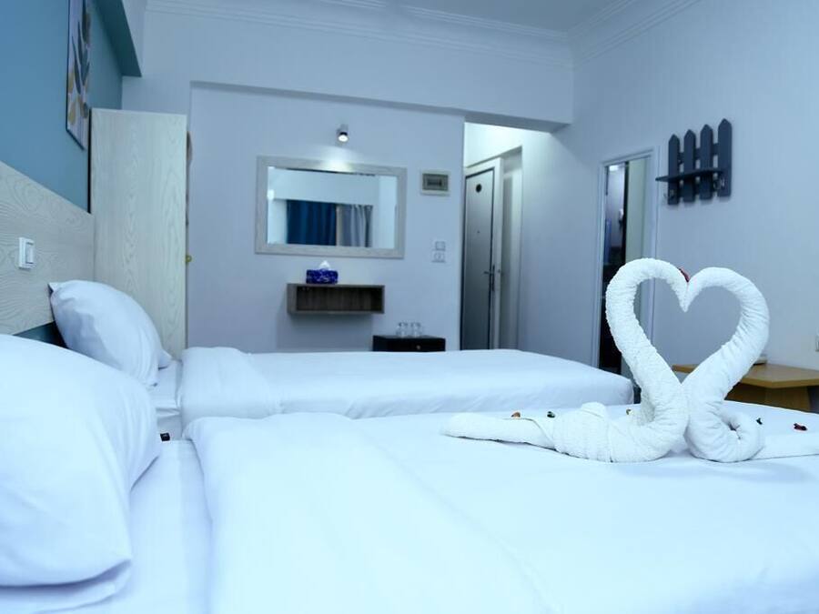 Ein Hotelzimmer mit zwei Betten, einem Spiegel, einer kleinen Ablage und einer herzförmigen Handtuchgestaltung.
