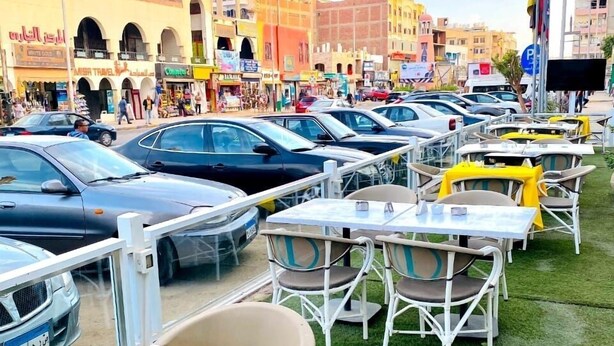 A parking lot with multiple cars and outdoor seating areas with tables and chairs. - Lamera Hotel. (Hurghada)