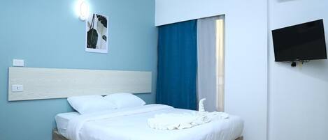 A hotel room with a bed, a flat-screen TV, and a wall-mounted air conditioner.