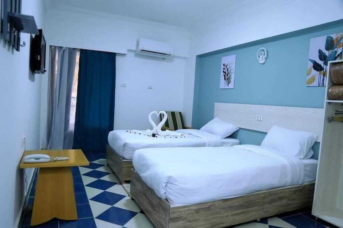 A hotel room with two beds, a wooden nightstand, a telephone, and a blue and white checkered floor.