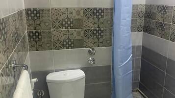 Ein Badezimmer mit Toilette, einer Dusche mit blauer Duschvorhang und Wandfliesen mit Muster.
