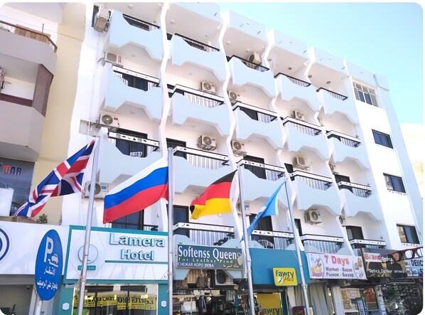 A multi-story hotel with balconies, a parking sign, and various storefronts including a hotel, a soft furnishings store, and a market. - Lamera Hotel. (Hurghada)
