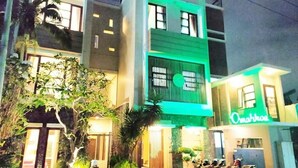 A multi-story building with a green-lit central section, a visible sign reading "Omahkox," and several motorcycles parked outside. - OYO 3939 Omahkoe Guest House Syariah (Malang)