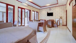 A spacious room with a large bed, a dining area with chairs, a TV mounted on the wall, and a refrigerator. - OYO 3939 Omahkoe Guest House Syariah (Malang)