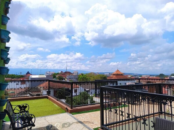Varanda com vista para a paisagem urbana, incluindo gramado verde e guarda-corpo de metal.
