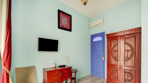 A room with a television, a desk, a chair, a blue door, and a decorative wooden door. - OYO 3939 Omahkoe Guest House Syariah (Malang)