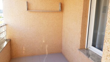 Un pequeño balcón con baranda de metal, una ventana que da a vistas exteriores y una pared con textura.